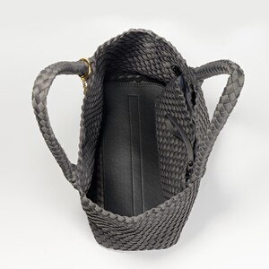 May include: A gray woven tote bag with braided handles and a gold-colored chain detail. The bag has a zippered pocket and a black interior. The tote is open, showing the inside of the bag.