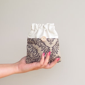 May include: A small, white drawstring bag with a brown and black patterned bottom. The bag has a wooden button closure.