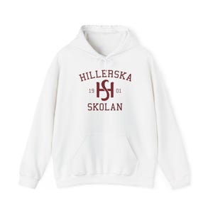 May include: White hoodie with a kangaroo pocket and drawstring. The front displays maroon text: "HILLERSKA SKOLAN", with "HS" in the centre and the numbers "1901". A casual, comfortable garment.