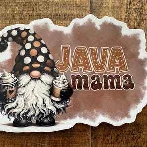 May include: A sticker featuring a gnome holding two coffee cups with whipped cream. The gnome wears a black hat with white and brown polka dots and has a long white beard. The words "JAVA mama" are printed on a brown background.