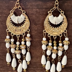 May include: Gold and white dangle earrings with a crescent moon design and white beads. The earrings have a delicate, feminine look.