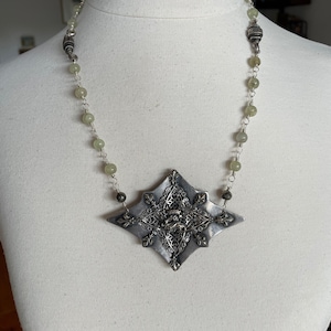 May include: A silver necklace with a large, ornate, silver pendant and green beads.