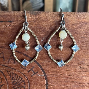 Puede incluir: Pendientes de plata con forma de lágrima. Los pendientes están hechos con pequeñas cuentas de plata y presentan una perla blanca y cristales facetados transparentes.