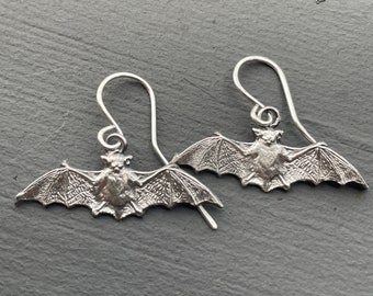 May include: A pair of silver bat earrings with detailed wings and a textured body.