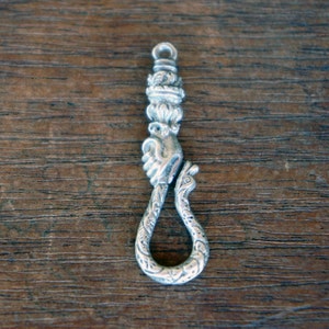 May include: A silver key chain with a detailed design of a hand holding a snake. The snake is curled into a loop, forming the key chain's ring.