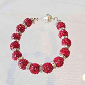 May include: A red crystal bracelet with a silver clasp. The bracelet is made of small, round beads that are covered in red crystals.