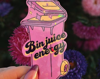 May include: A pink sticker shaped like a bin, with the words "Bin juice energy". The bin has a yellow lid and sparkles. The sticker is held against a backdrop of colourful flowers, including pink, purple, and blue blooms.