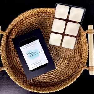 May include: A black box of White Linen Clean Laundry 100% Natural Soy Wax Melts, hand poured in Houston, TX. The box is sitting on a woven basket with a clear plastic tray of six white wax melts.