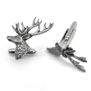 May include: A pair of silver-toned metal cufflinks featuring a detailed three-dimensional stag head design with prominent antlers. The cufflinks have a polished finish and a standard toggle closure mechanism on the back for securing to a shirt cuff.