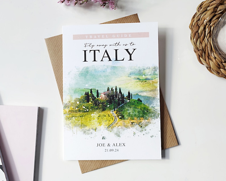 May include: A watercolour illustration of a Tuscan landscape with a house and rolling hills. The text "TRAVEL GUIDE" is at the top of the card, and the text "Fly away with us to ITALY" is below it. The text "JOE & ALEX 21.09.24" is at the bottom of the card.