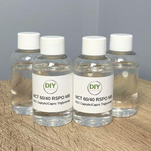 Op de afbeelding: Vier heldere flessen met witte doppen, gevuld met een transparante vloeistof. Elke fles heeft een etiket met de tekst "DIY" en "MCT 60/40 RSPO MB". De etiketten bevatten ook "INCI: Caprylic/Capric Triglyceride".