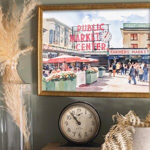 Callaghan Collective Watercolor Painting of Pike Place Market in Seattle Washington featuring the Public Market Center sign, red umbrellas, and the Farmers Market crowd, Pacific Northwest wall art for apartment or office decor.