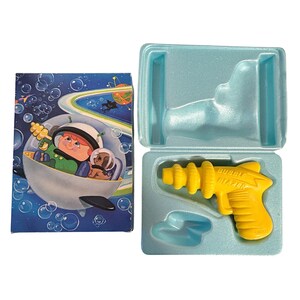 May include: A vintage yellow plastic Bubble Blazer toy gun in a light blue plastic case. The case is open, revealing the toy gun and a small blue plastic piece. A colorful illustration on the box shows a cartoon astronaut in a bubble.