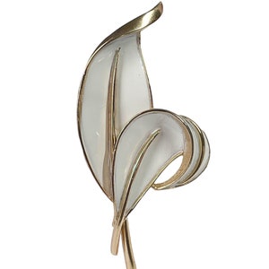 May include: A gold-toned brooch with two white enamel leaves. The leaves are stylized and have a delicate, feminine look.