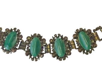 May include: A gold tone bracelet with four oval green stones set in ornate floral designs. The bracelet has a clasp closure.