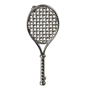 May include: A silver tennis racket brooch with a detailed wire mesh design. The handle is twisted and has a small loop at the top for attaching to clothing.