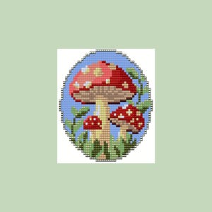 May include: A cross-stitch design of three red and white mushrooms with brown stems and green leaves, set against a light blue background. The design is framed by a blue border and set on a light green background.