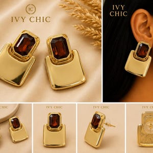 May include: Gold-toned earrings featuring a rectangular, deep red faceted gemstone set above a smooth, polished gold-toned metal plate. The earrings are branded with the text IVY CHIC and include a clear plastic backing for the post.