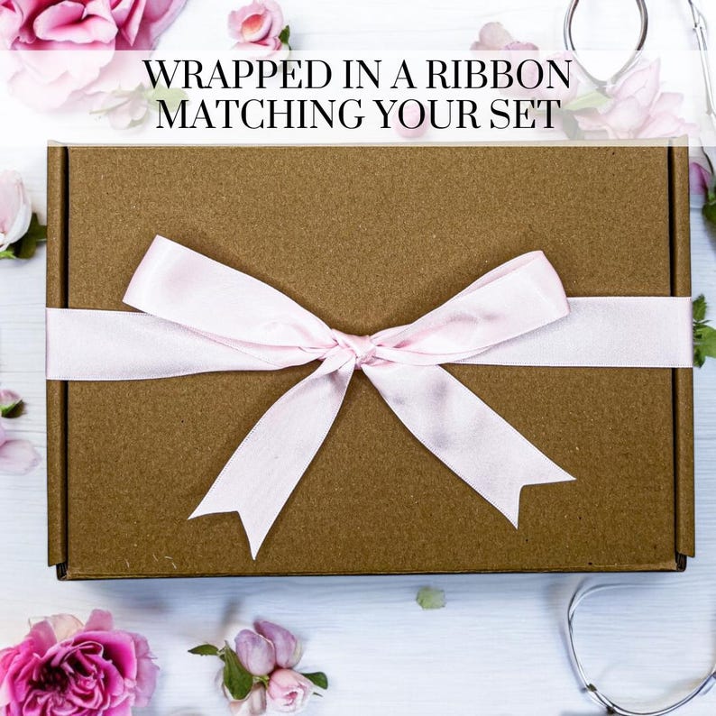 May include: A brown cardboard box with a pink ribbon tied in a bow. The box is sitting on a white surface with pink flowers scattered around it. The text "WRAPPED IN A RIBBON MATCHING YOUR SET" is printed on the top of the image.