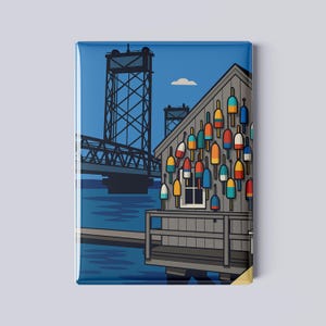 May include: Rectangular magnet featuring a coastal scene. A gray wooden building is adorned with colorful buoys. A blue bridge spans the background under a blue sky. The artwork has a flat, graphic style.