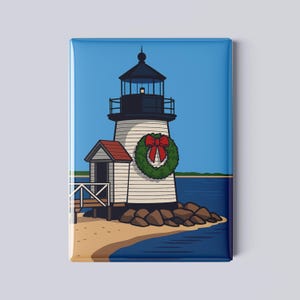 May include: A rectangular magnet featuring a cartoon illustration of a lighthouse on a sandy shore. The lighthouse is white with black accents and a red-bowed wreath. A small wooden structure and the ocean are also visible.