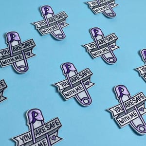 May include: Multiple white embroidered iron-on patches with a purple safety pin and the text "You are safe with me" and a small heart.