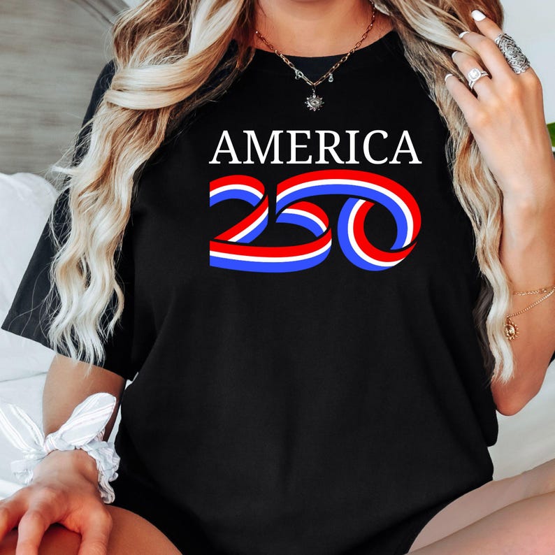 Może przedstawiać: Czarny t-shirt z napisem "AMERICA" w kolorze białym. Poniżej liczba "250" zaprojektowana z czerwonych, białych i niebieskich wstążek. Koszulka ma swobodny styl.