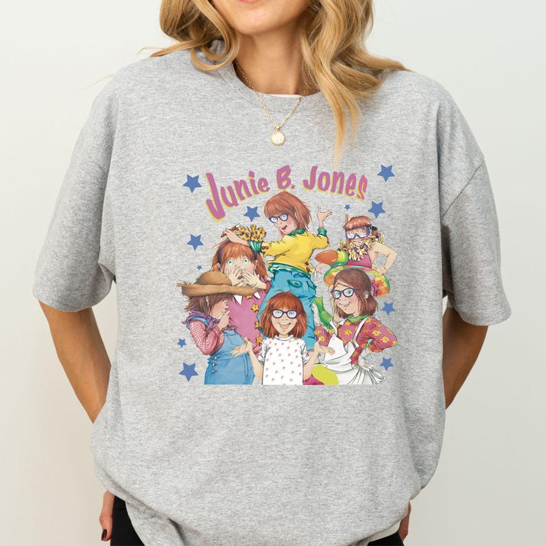 Op de afbeelding: Grijs T-shirt met een grafische print van de personages uit het boek "Junie B. Jones" van Barbara Park. De afbeelding toont Junie B. Jones en haar vrienden.