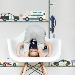 May include: A child is standing upside down in a white chair in front of a wall with police car decals. The decals feature a police car, a police van, and a stop sign. The decals are on a gray road with yellow lines.