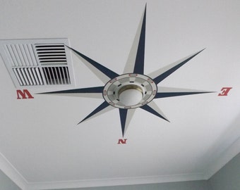 May include: A white ceiling with a painted compass design in blue and white. The compass points are labeled with the letters N, S, E, and W in red.