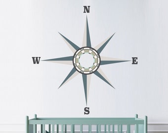 May include: A light blue crib with a white mattress and a white and gray compass wall decal with the letters N, S, E, and W.