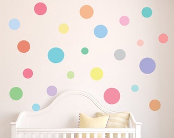May include: A white crib with a white ruffle skirt and a purple rug. The wall behind the crib is decorated with colorful polka dot stickers in various sizes.