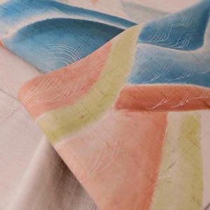 Può includere: Primo piano di un tessuto con un motivo geometrico in tonalità di blu, verde e arancione. Il tessuto ha una texture sottile e un aspetto morbido e sbiadito.