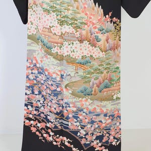 May include: Black kimono with a colorful floral and landscape design. The design features a mountain scene with trees, flowers, and a bridge. The kimono is made of silk and has a traditional Japanese pattern.