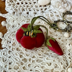 May include: A deep red velvet tomato pincushion with a green felt stem and a small embroidered bee, attached by green cords to a smaller red velvet strawberry-shaped emery and a pair of ornate, antique-style brass metal embroidery scissors.