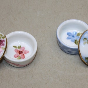 Peut inclure: Deux petites boîtes à bijoux en porcelaine avec couvercles. Une boîte est décorée de fleurs roses et blanches, l'autre de fleurs bleues et blanches.