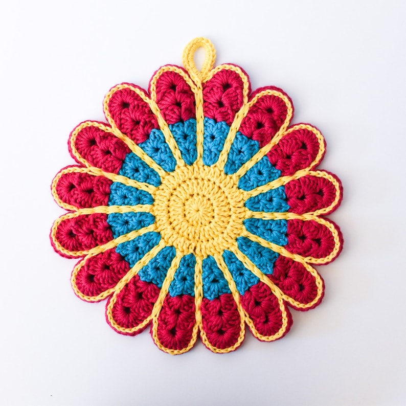 May include: A crocheted flower-shaped hot pad in red, yellow, and blue. The hot pad has a circular center and petals that extend outward.