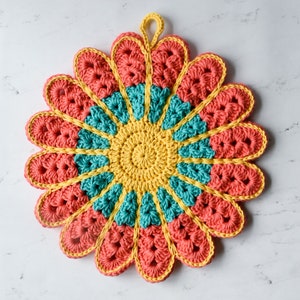 May include: A crocheted flower-shaped pot holder in shades of yellow, teal, and coral. The pot holder has a loop for hanging.