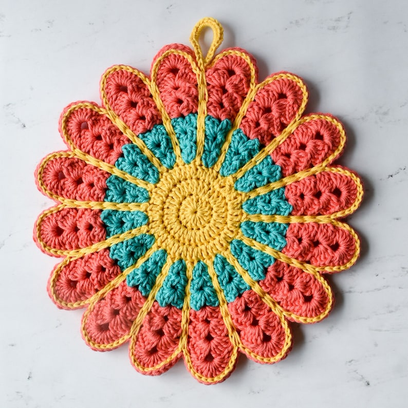 May include: A crocheted flower-shaped pot holder in shades of yellow, teal, and coral. The pot holder has a loop for hanging.
