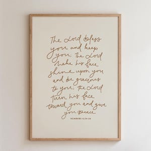 Puede incluir: Una impresión enmarcada con un fondo beige claro y escritura marrón. El texto dice "El Señor te bendiga y te guarde..." de Números 6:24-26. El marco es de madera clara.