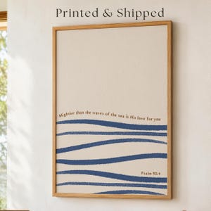 May include: A vertical rectangular wall art piece in a light wood frame featuring a beige background with dark blue horizontal wavy lines. The text "Mightier than the waves of the sea is His love for you" and "Psalm 93:4" are printed in brown.