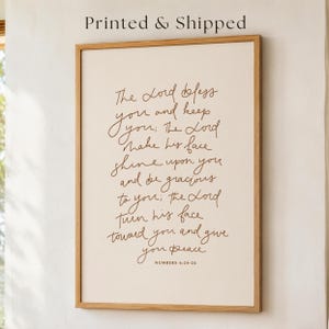 May include: A rectangular wall art print in a light oak wood frame featuring the text: The Lord bless you and keep you; The Lord make his face shine upon you and be gracious to you; the Lord turn his face toward you and give you peace. NUMBERS 6:24-26.