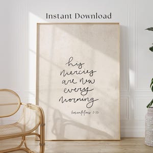 May include: A framed print with the words "his mercies are new every morning" in black script. The print has a beige background and the text "Instant Download" at the top. A wicker chair is in the foreground.