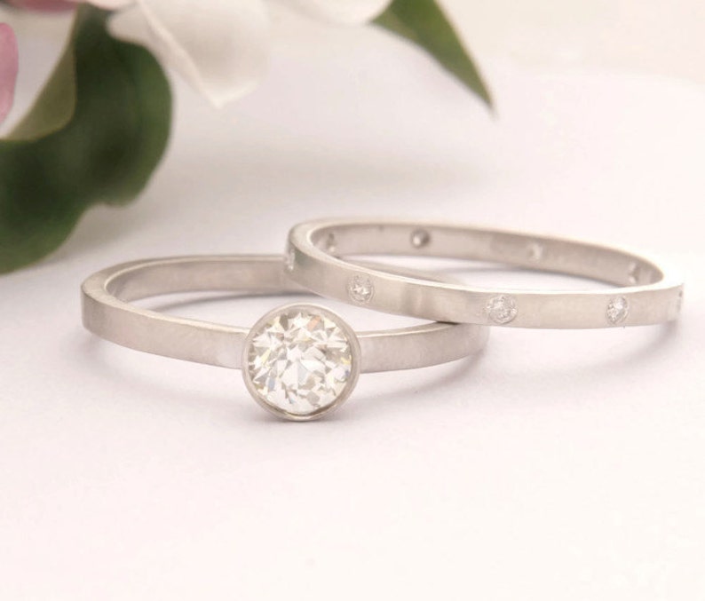 Może przedstawiać: Zestaw dw&oacute;ch srebrnych obrączek ślubnych. G&oacute;rna obrączka ma jeden okrągły diament osadzony w oprawie typu bezel. Dolna obrączka ma rząd małych diament&oacute;w osadzonych w oprawie typu bezel.
