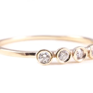 Puede incluir: Un anillo de banda de oro con cuatro pequeños diamantes redondos engastados en fila.