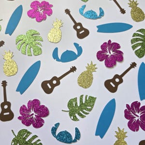 Peut inclure: Un assortiment de formes découpées colorées et scintillantes sur fond blanc. Les formes comprennent des planches de surf bleues, des ukulélés bruns, des ananas dorés, des fleurs d'hibiscus roses, des feuilles de monstera vertes et des formes de personnages bleus. Le thème est tropical.