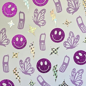 May include: A collection of purple glitter stickers in various shapes, including smiley faces, butterflies, cell phones, stars, and lightning bolts. The stickers have a shiny, reflective surface and are scattered across a white background.