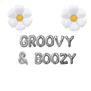May include: Two white daisy-shaped balloons with yellow centers are positioned above silver foil letter balloons spelling "GROOVY & BOOZY". The balloons are arranged on a white background.