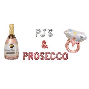 Op de afbeelding: Een set van roze gouden en zilveren folie ballonnen die "PJS & PROSECCO" spellen met een roze gouden ring ballon en een fles roze champagne.
