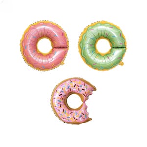 May include: Three donut-shaped foil balloons. One is pink with sprinkles, one is green with sprinkles, and one is pink with sprinkles and a bite taken out of it.